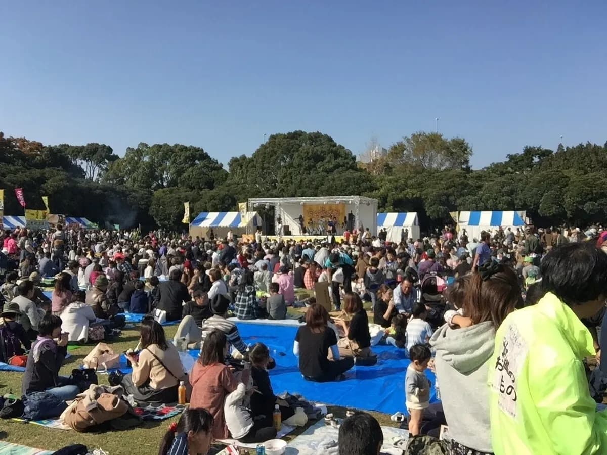 芝生の会場に大勢の来場者が集まる、野外ステージのある催事